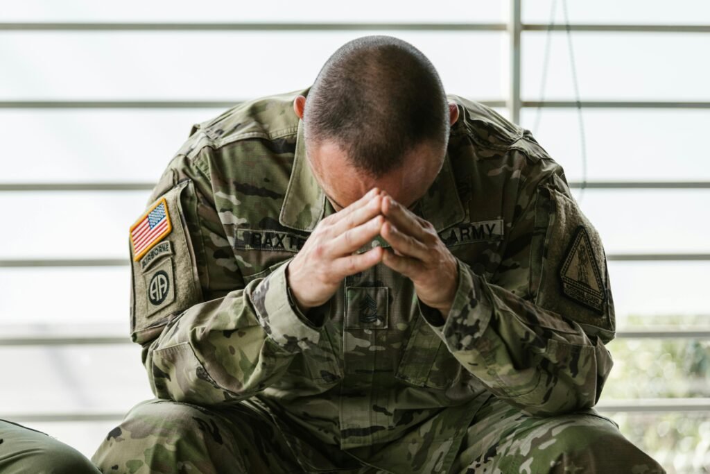 U.S. Army soldier in uniform sitting with head in hands, showing emotional stress after an off-duty military injury