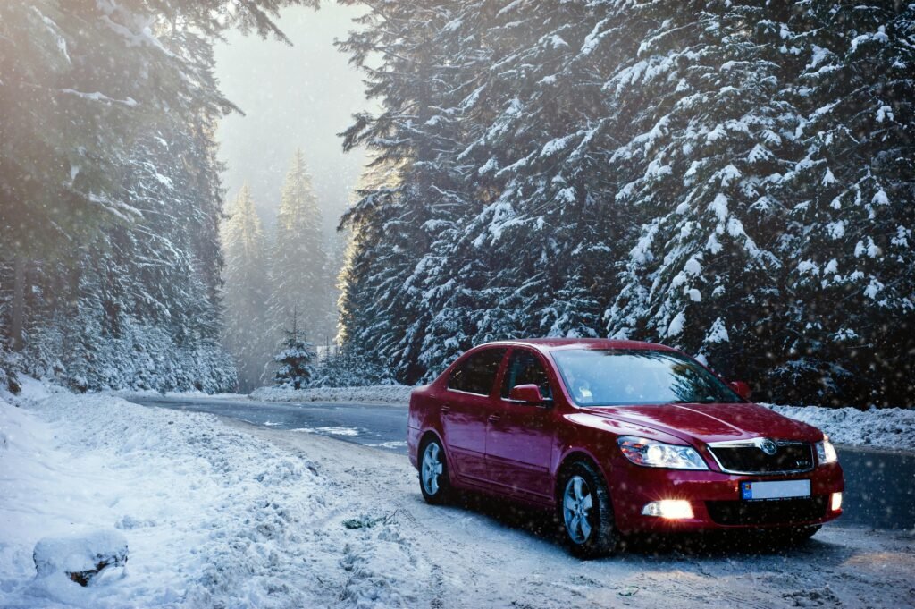 Alt Text Red car driving through snowy road conditions, highlighting winter driving tips and the importance of preparation in icy weather.