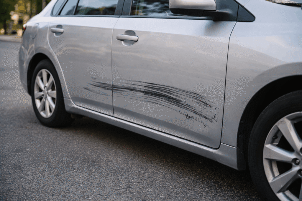 Minor car crash showing a tire mark and light side damage on a silver sedan after a low-speed collision